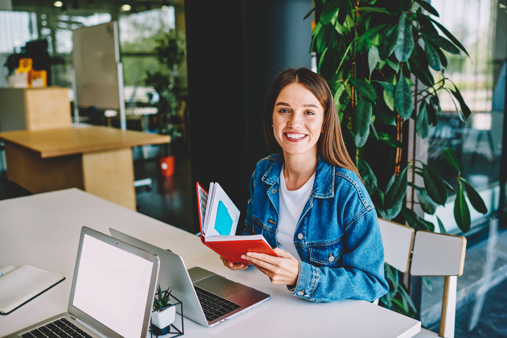 Portrait,Of,Cheerful,Female,Student,With,Education,Notepad,Sitting,At
